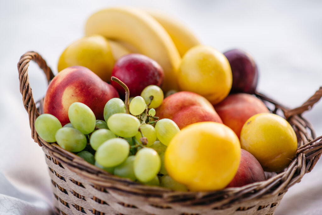 Wicker basket filled with fresh grapes, bananas, nectarines, and plums, styled as a healthy get well soon fruit basket or natural gift hamper in Singapore.