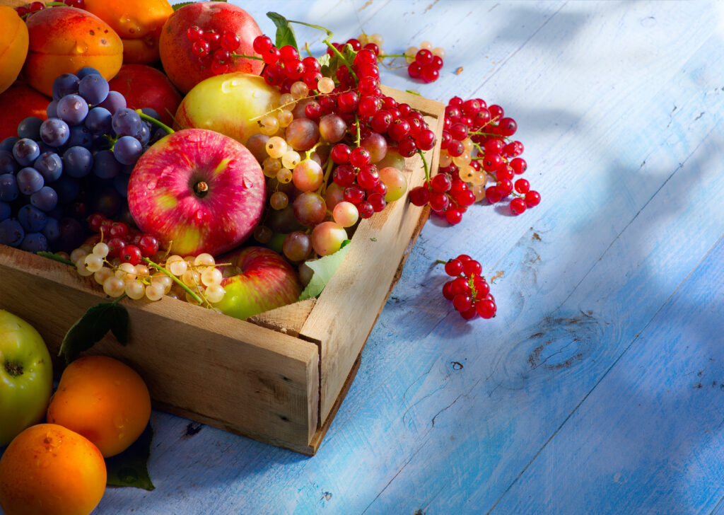 Wooden crate filled with fresh apples, grapes, apricots, and berries, styled as a colourful get well soon fruit basket or healthy gift hamper in Singapore.